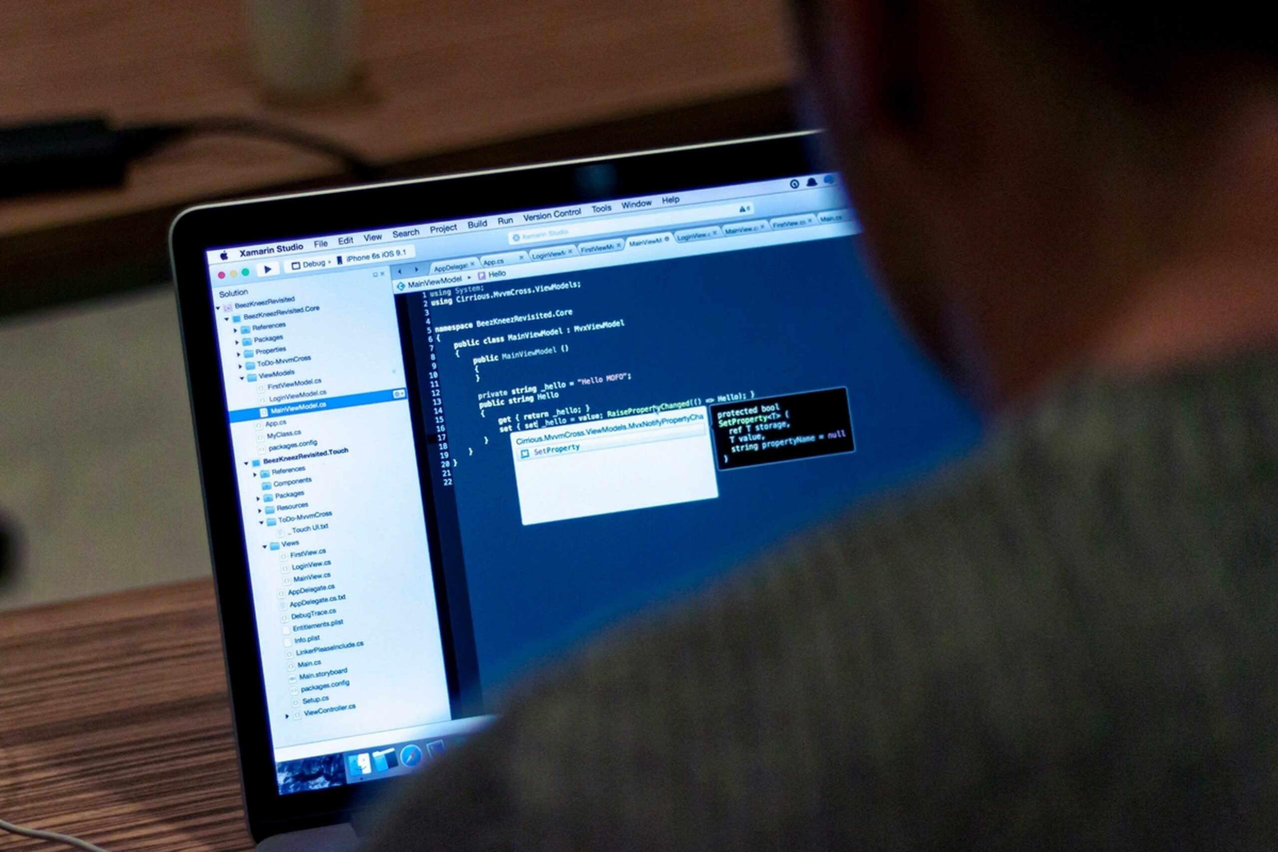 Programmeur kijkt over de schouder naar broncode in een ontwikkelomgeving op een laptop.